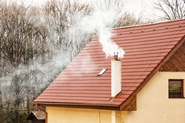 casa con camino che fuma, la canna fumaria emette fumo bianco e grigio